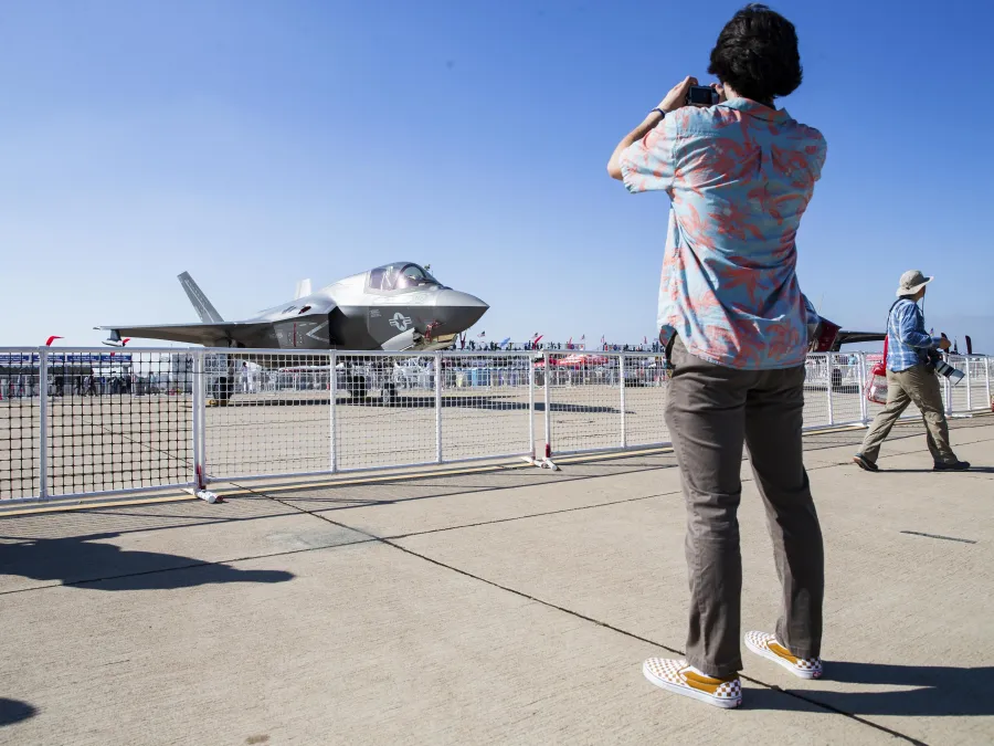 A person in a patterned shirt takes a photo of a military jet at the MCAS Miramar Air Show in San Diego.