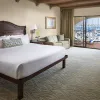 Hotel room with a neatly made bed, sofa, framed artwork, and sliding glass doors leading to a balcony overlooking a marina with boats.