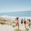 Group of friends joyfully running towards the beach under a clear blue sky.