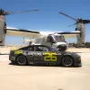 A sleek black NASCAR racing car with the number 26 is parked in front of a U.S. Navy Osprey aircraft on a sunny day at Naval Base Coronado near San Diego.