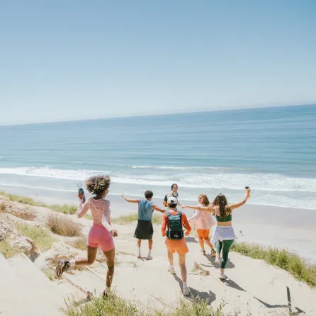 Group of friends joyfully running towards the beach under a clear blue sky.