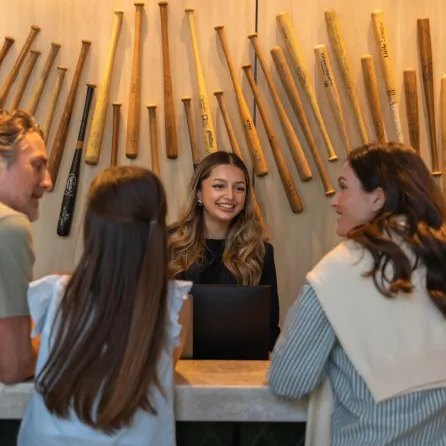 A friendly receptionist at the Omni in San Diego assists two guests at a modern front desk with wooden decor.