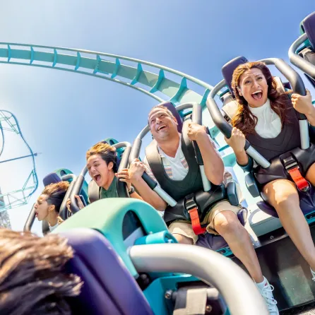 Five people joyfully ride the Emporer roller coaster, expressing excitement against a blue sky in San Diego.