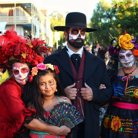 Four people in traditional Dia de los Muertos costumes, smiling, with colorful makeup and decorations.